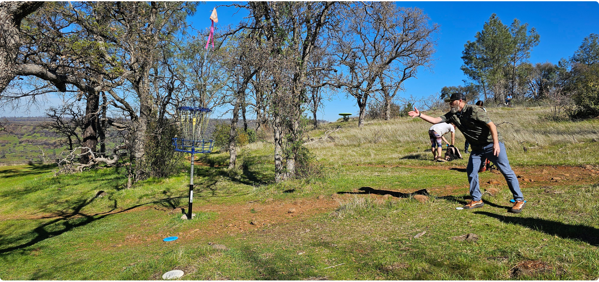 A man throwing a disc golf towards a basket that is using a Disc Golf Riser