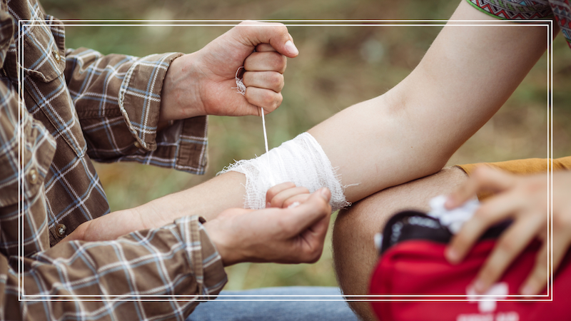 A person wrapping his friends arm in gauze holding a adventure medical kit